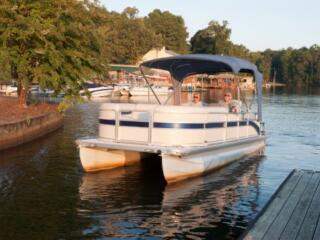 white pontoon boat with raised cover sitting in the water near dock