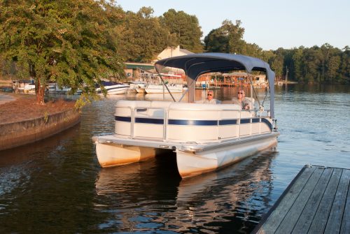 white pontoon boat with raised cover sitting in the water near dock