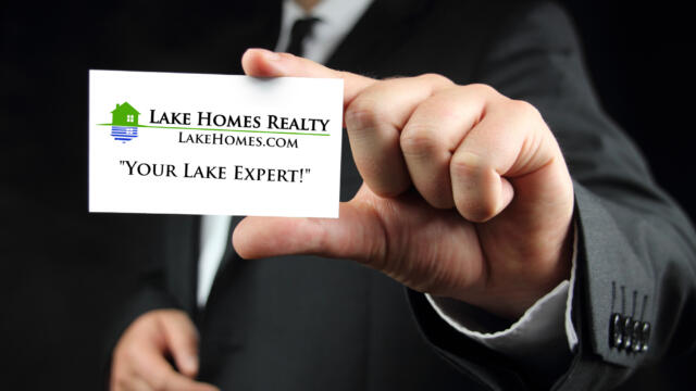 man in a suit holding out a Lake Homes Realty Lake Expert