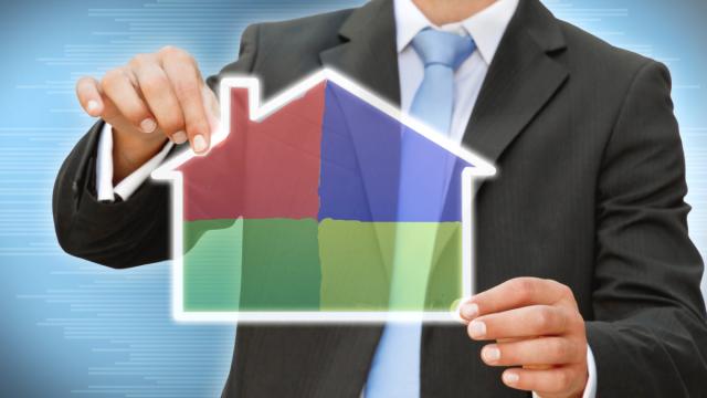 man in suit holding an outline of a house, filled with colored panes.