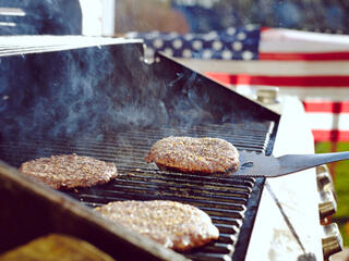 hamburgers cooking on a grill in front of an american flag