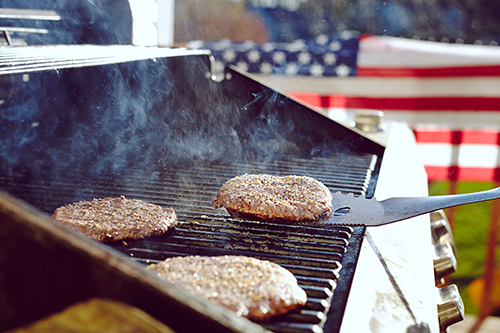 hamburgers cooking on a grill in front of an american flag