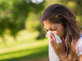 woman outside on a sunny day sneezing into a tissue