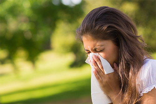 woman outside on a sunny day sneezing into a tissue