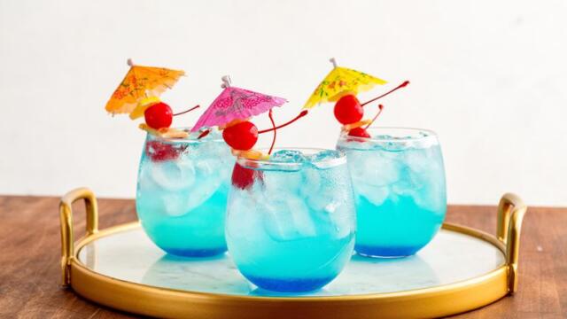 3 glasses of blue mermaid lemonade cocktails with cherries and mini umbrella garnishes