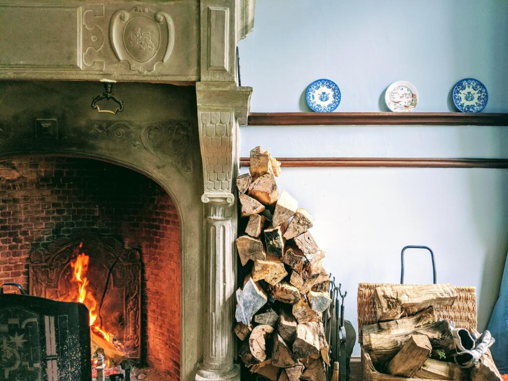 Pile of chopped firewood leaning against lit wood fireplace