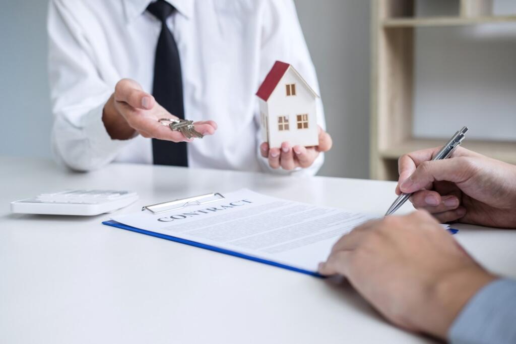 Person holding house and keys in hand while homebuyer signs leased land contract