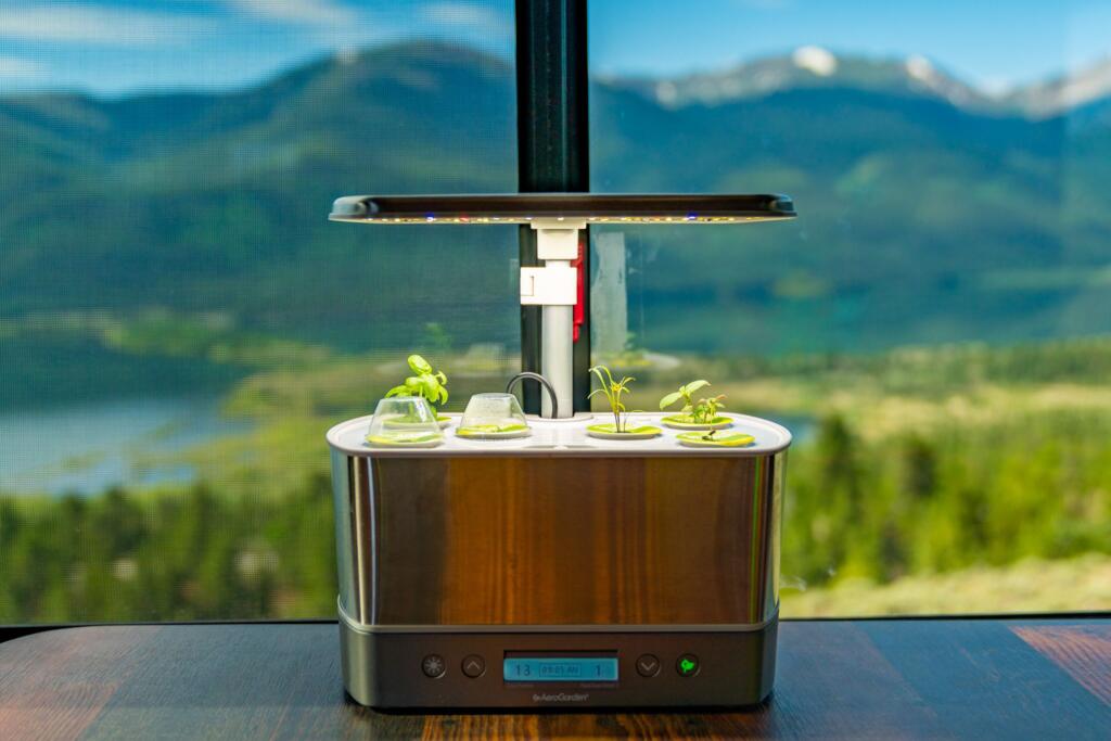 Aerogarden Harvest Elite---an indoor gardening sytem---sitting in an RV with mountains and a lake in the background.