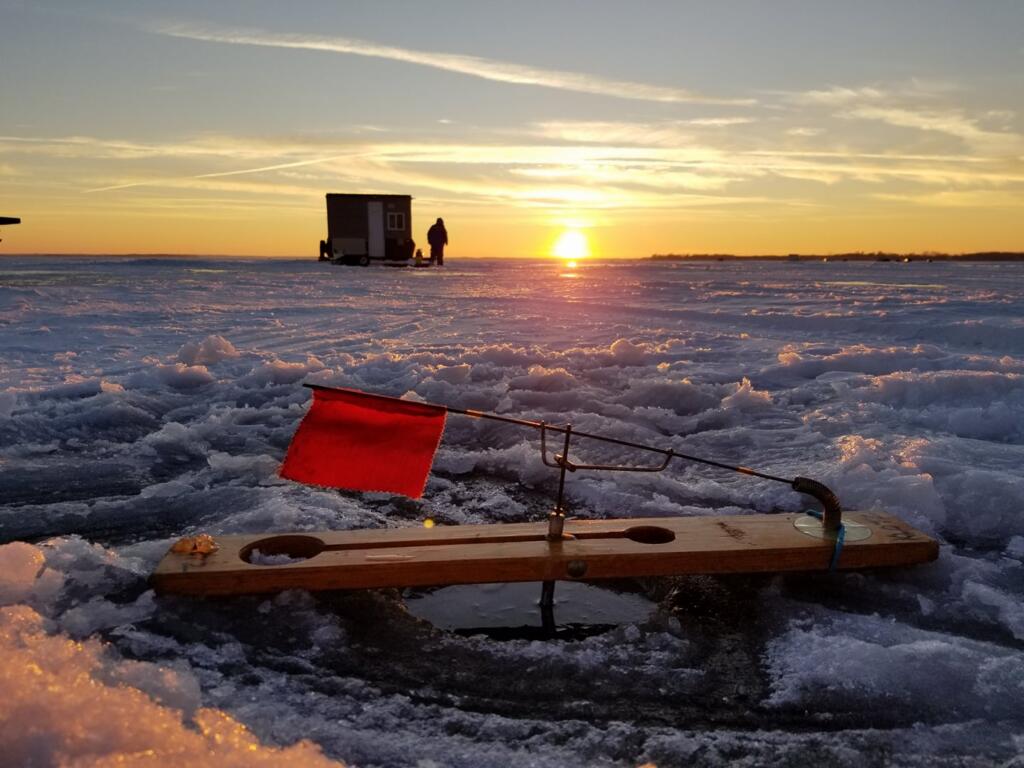 A tip-ups---a device used to catch fish in ice fishing---over the hole with a sunset in the background.