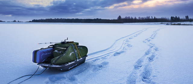 A sled with tarp straps on top of a frozen lake with trees and a sunset in the background. 