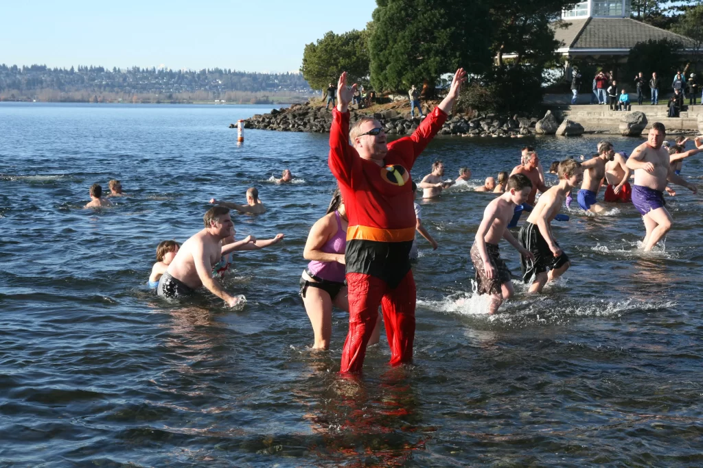Man standing in Lake Sammamish dressed up in an Incredibles costume with children in the background, all taking part in the polar plunge. 