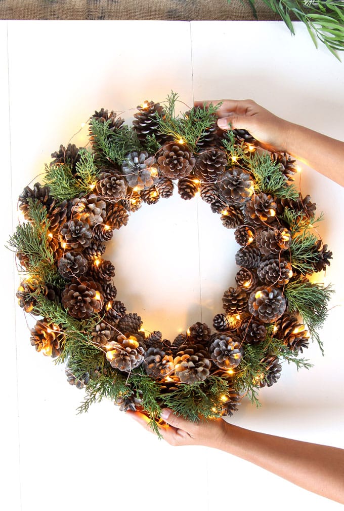 DIY holiday wreath filled with pine cones, lights, and greenery.