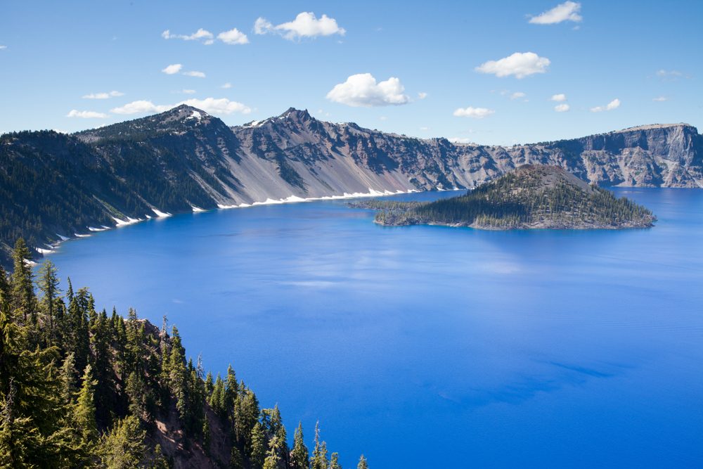 Crater Lake in Oregon, sparkling blue waters with grey mountains and green trees around. 