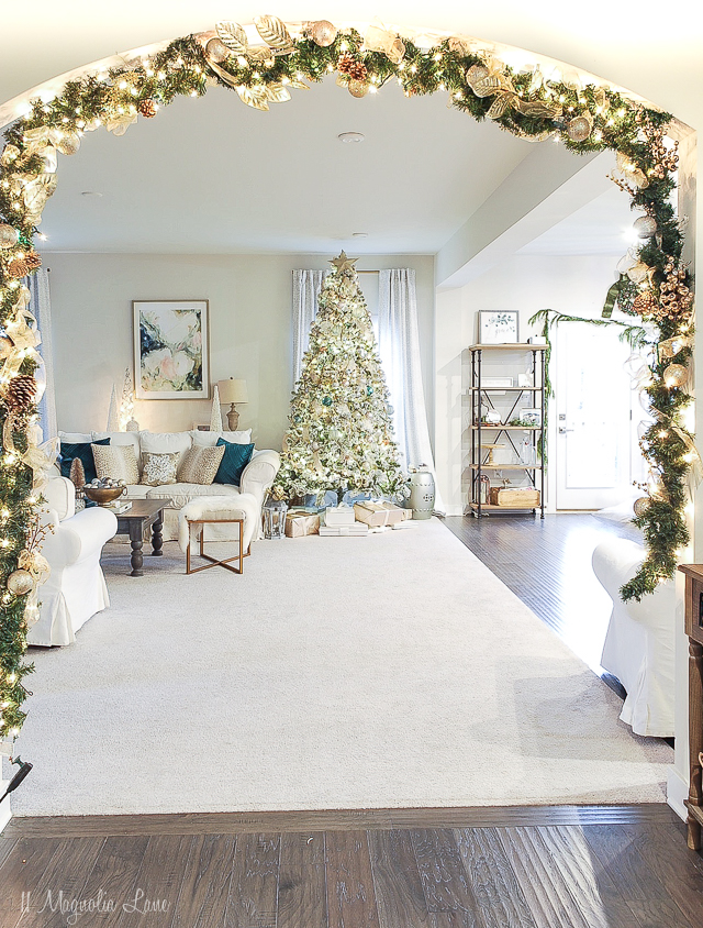 Elegant DIY Christmas garland, filled with gold embellishments and ribbon in front of a living room with a Christmas tree inside. 