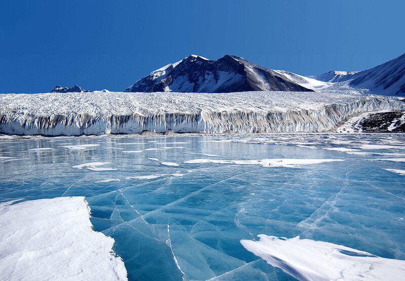 Frozen lake in Antarctica with snowy mountain in background. 