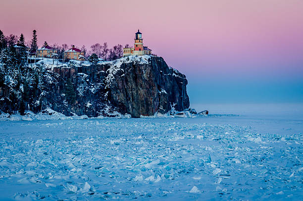 Split Rock Lighthouse, Minnesota pictured next to a snowy frozen lake and a pink sunset. 