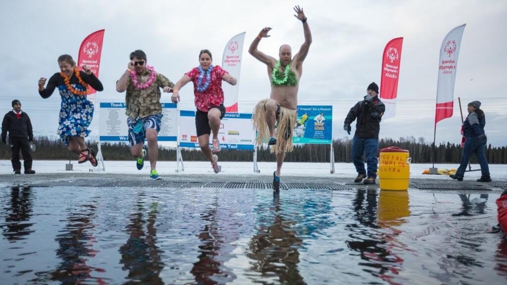 4 persons dressed in Hawaiian outfits jumping into a freezing lake for a polar plunge.  