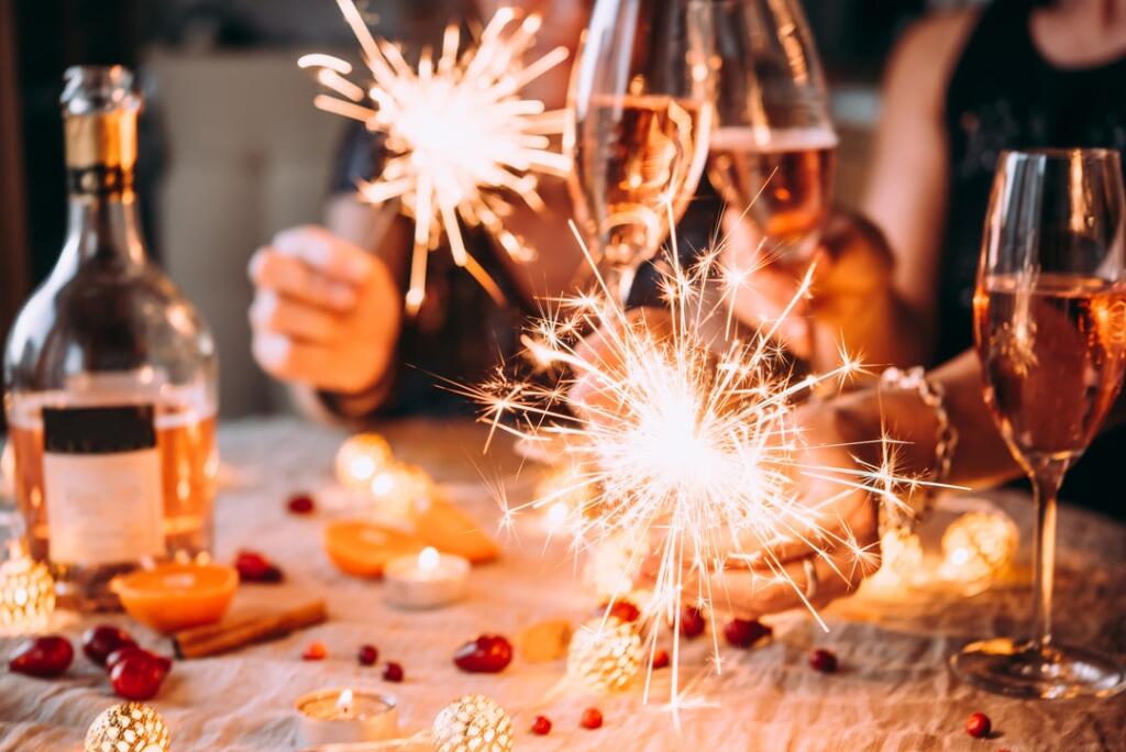 Hands clinking glasses of champagne together with sparklers in the frame. 
