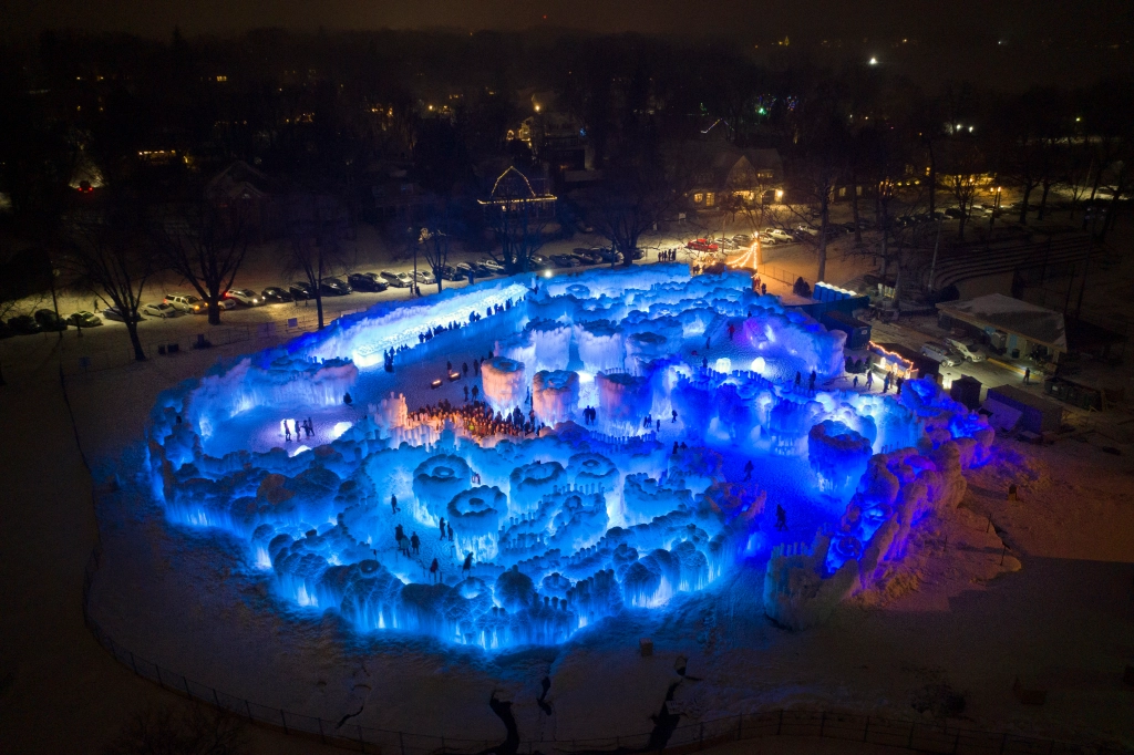 Aerial shot of ice castle at night, lit by blue LED lights and filled with visitors. 