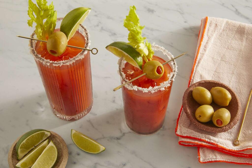 Classic Bloody Mary cocktails with salted rims, green olives, celery, and lime garnishes. 