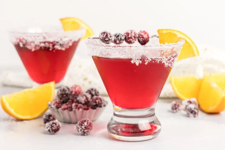 Crantinis beside sugared cranberries and orange slices. 