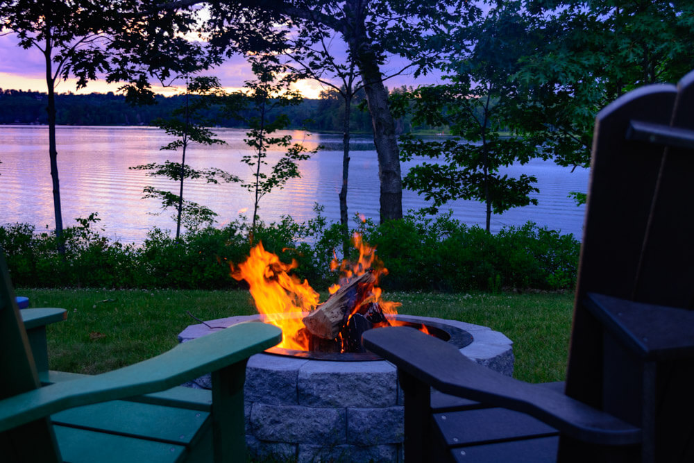 Firepit by lake with a sunset in the background. 