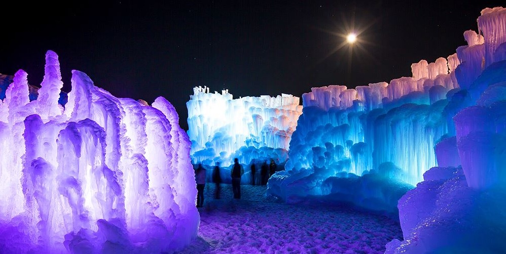 Tall ice structures lit by blue and purple lights at night.