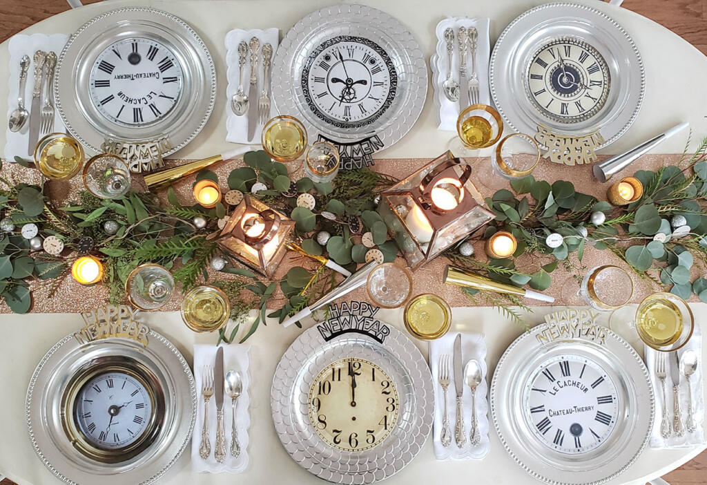 Table setting for a New Year's Eve party, complete with clock décor, gold cups, greenery, and silverware.
