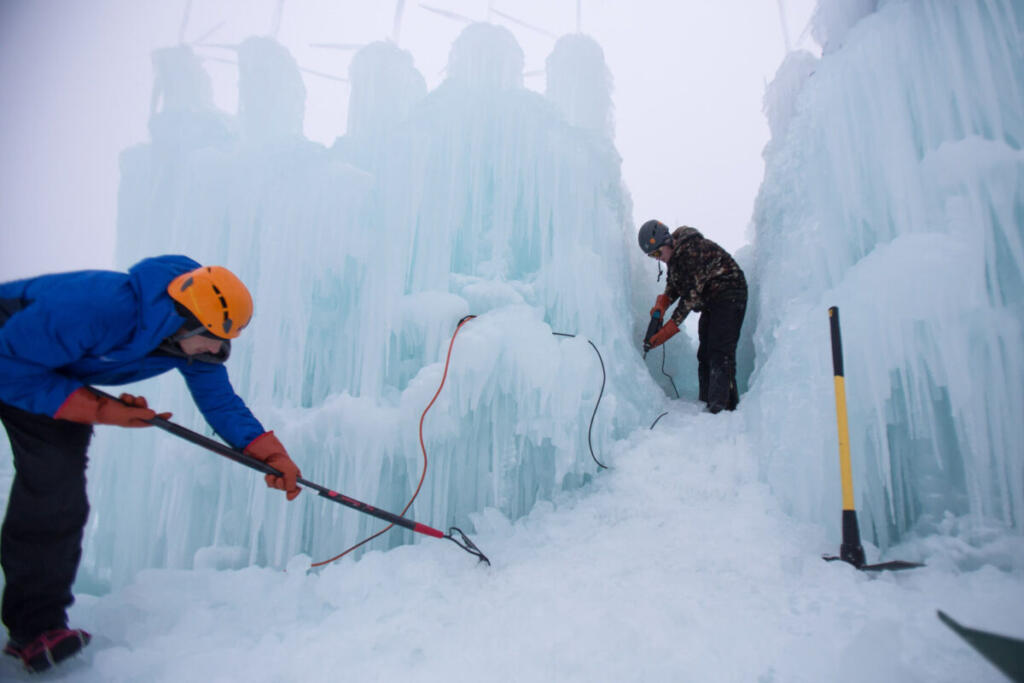 Men with hard hats dressed in winter clothes using tools to sculpt ice.