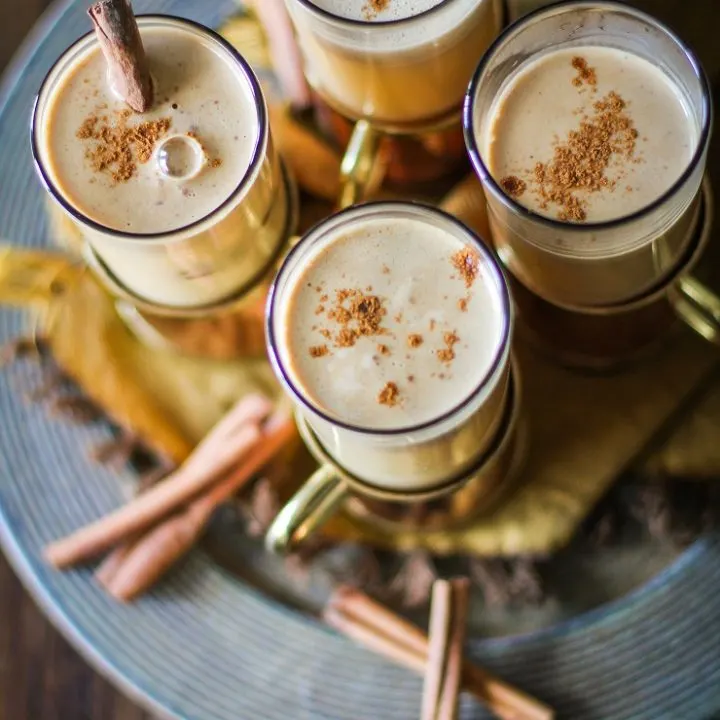 Frothy buttered rum cocktails in mugs topped with cinnamon.