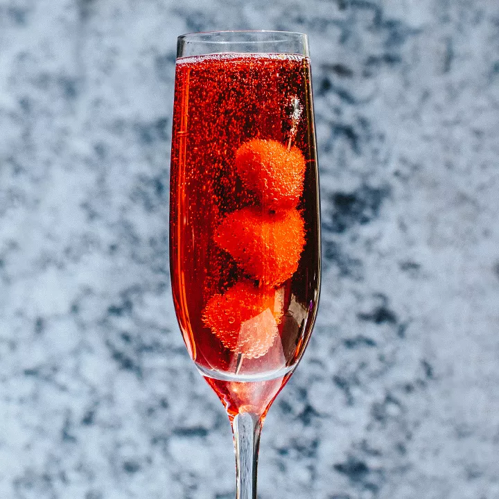 Red drink in champagne flute with skewered raspberries. 