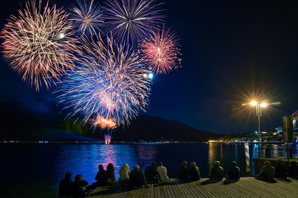 Fireworks over the lake at night as a crowd of people watch from the dock. 