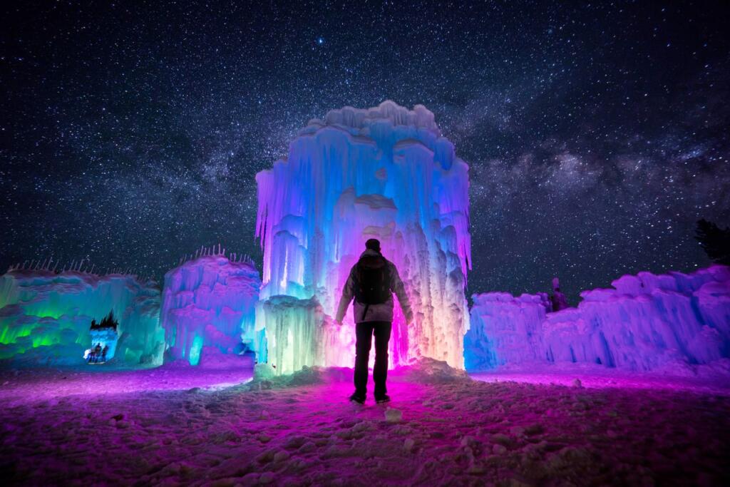 Man standing in front of a colorful ice castle at night. 