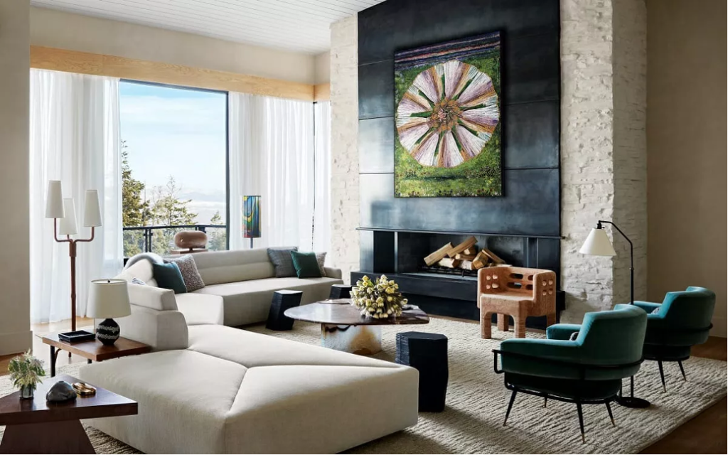 Living room with white brick fireplace,  teal-tinged metal fireplace surround, green abstract artwork, teal retro club chairs, cream sectional sofa, organic-shaped stone coffee table, textured area rug, natural wood accents