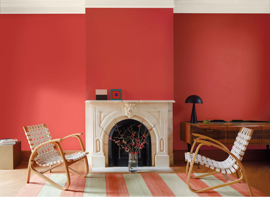 Benjamin Moore's Color of the Year Raspberry Blush walls with ivory marble fireplace surround, woven bentwood-style retro chairs, red and white striped rug, black lamp