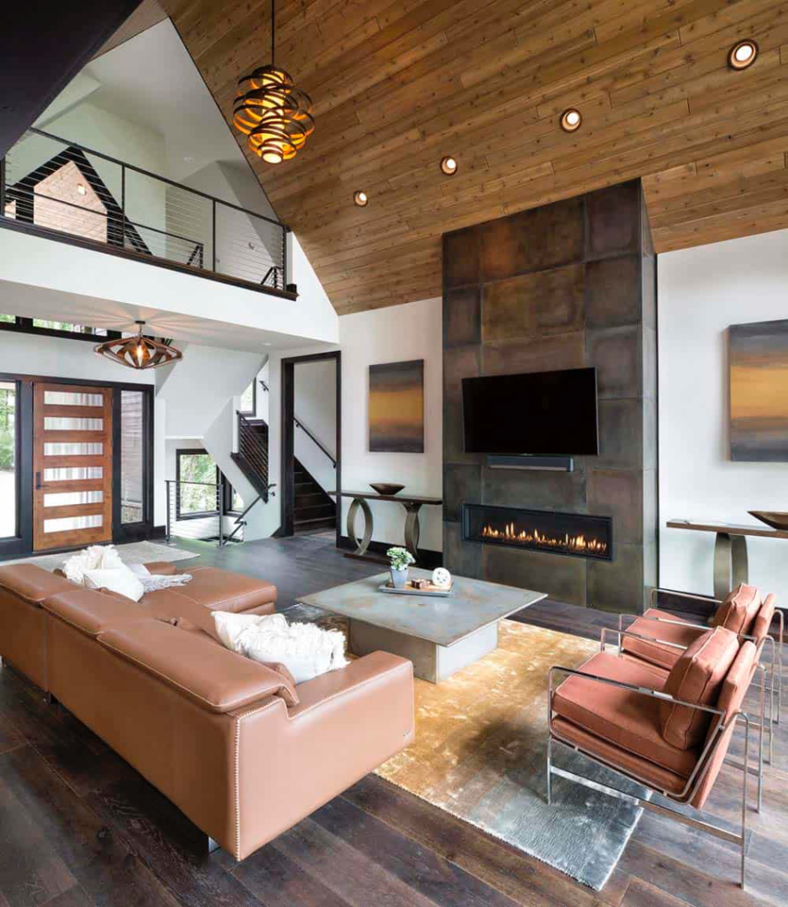 Living room with earthy elegance in finishes made of metal fireplace surround, wood slatted ceiling, stone coffee table, glass, leather sectional, plush area rug, abstract artwork