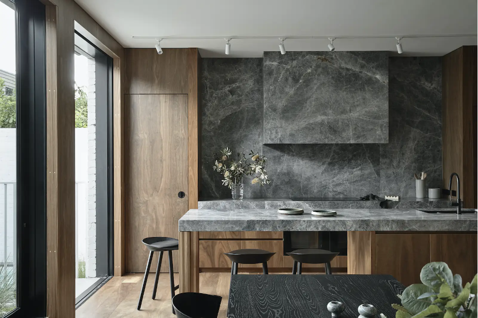 modern kitchen with dark gray marble with white veining that covers island surface, countertops, backsplash, and range hood. Wood cabinetry and timber joinery on island, dramatic, dark, moody vibe