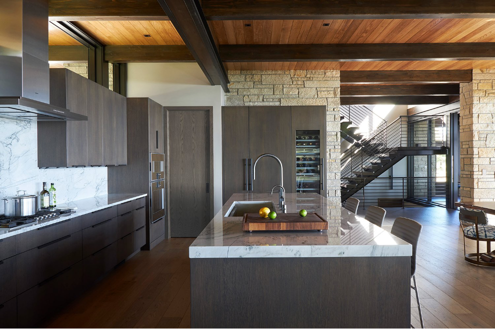 modern kitchen with marble backsplash, marble island, charcoal cabinetry, rustic brick walls, plank wood ceiling feature with dark-stained beams