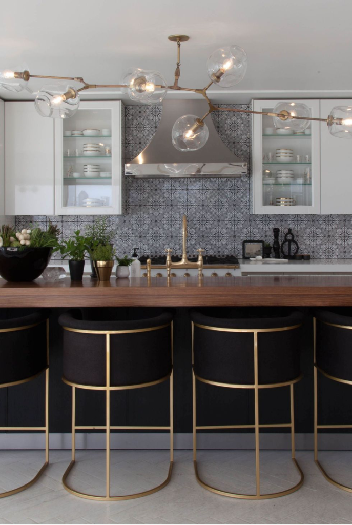 Mixed metal hardware in modern kitchen, gold trimmed metal counter stools, stainless steel range hood, gold faucet fixtures, glass orb mult-tiered lighting fixture over wood island, flower pattern tile backsplash