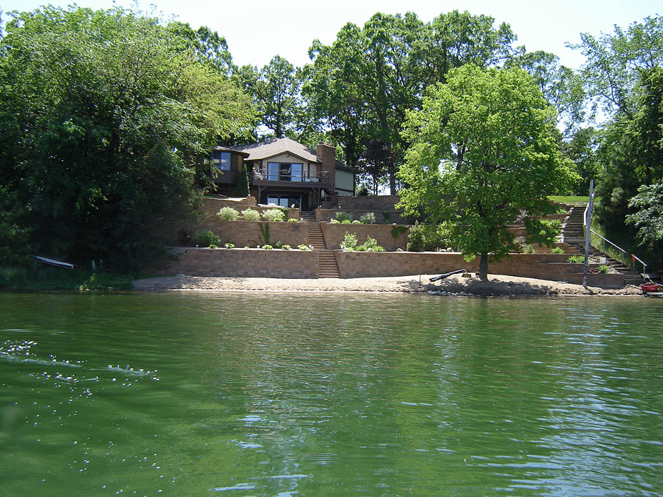 lake home seen from the water with tiered landscaping and steps leading to the back yard