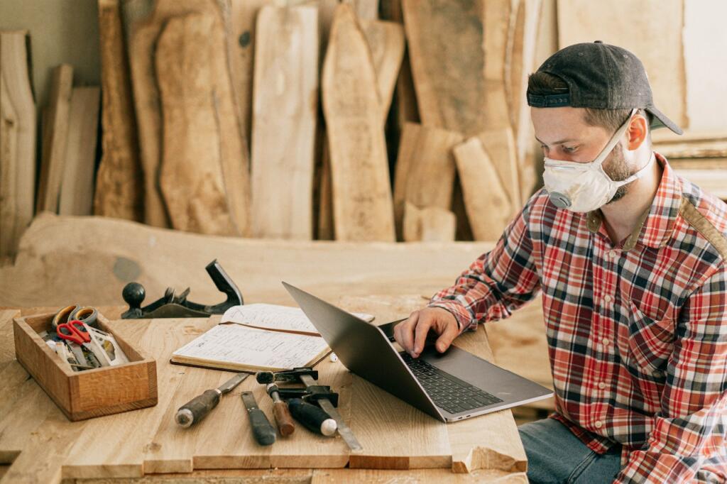 man in a workshop with tools, wood, a laptop, and a book