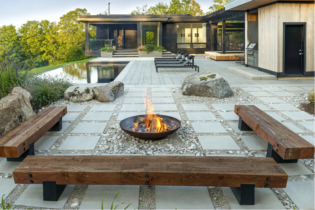 patio with stone pavers, rocks, gravel, wood benches, fire pit, and pool for lake landscape