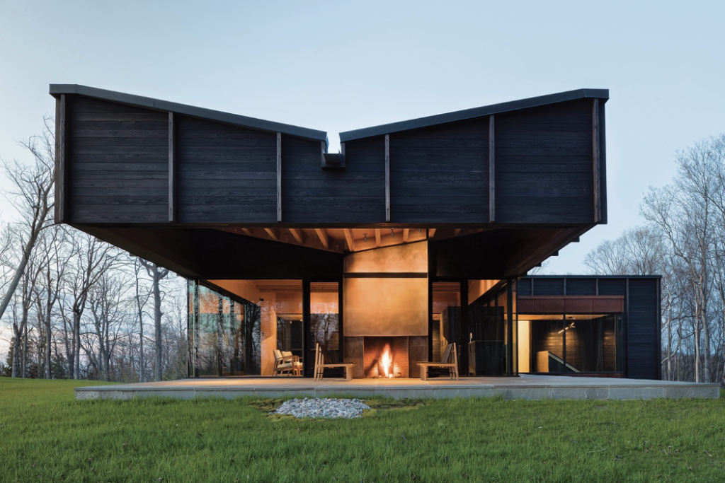 Undulating roofscape of charred cedar home and view of outdoor fireplace and patio