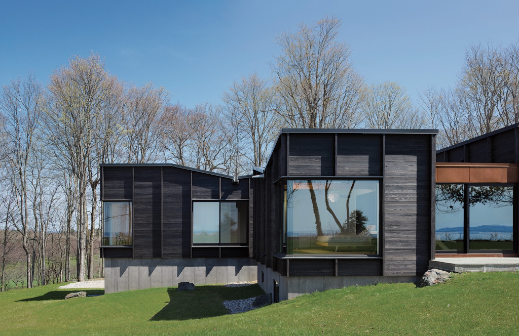 Exterior view of charred cedar home with reflections of the lake and landscape in windows