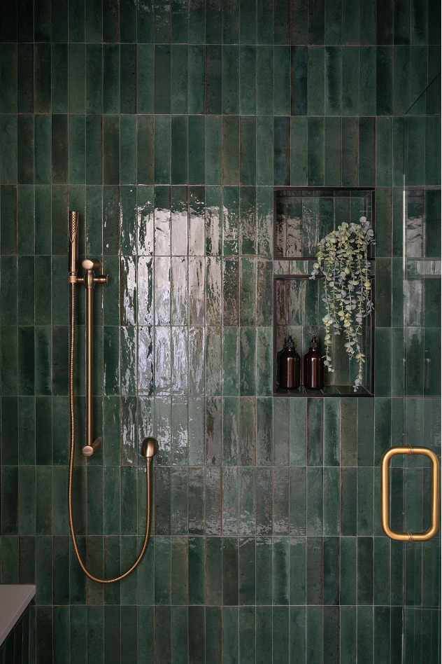 green-tiled shower wall with brass hardware accents and built-in shelving