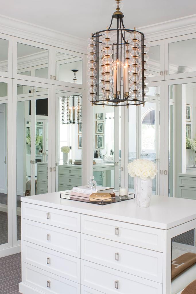 glamorous white walk-in closet with mirrored cabinetry, white cabinetry with silver hardware, and drum-shaped chandelier