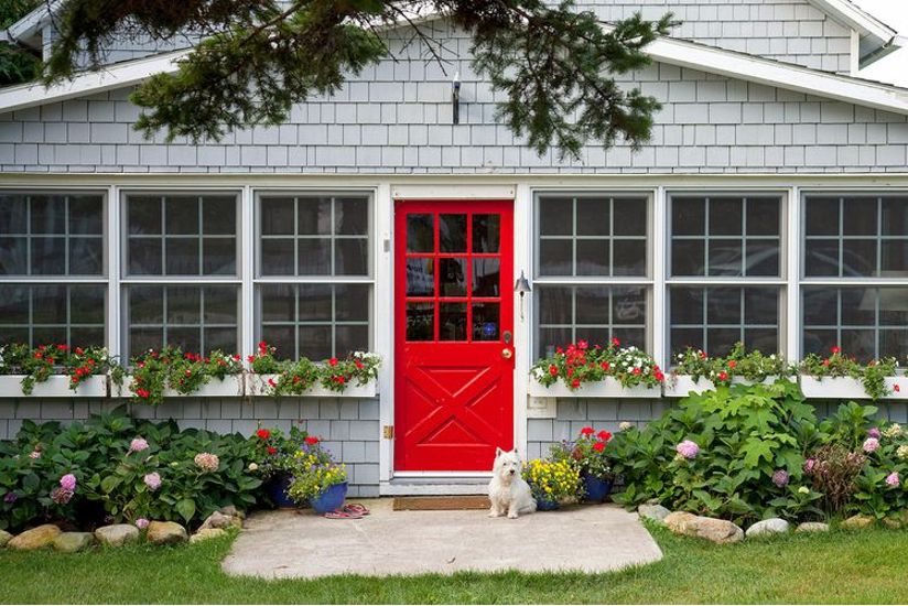 front facade with bright red door, window flower boxes, landscaping, stones, little white dog