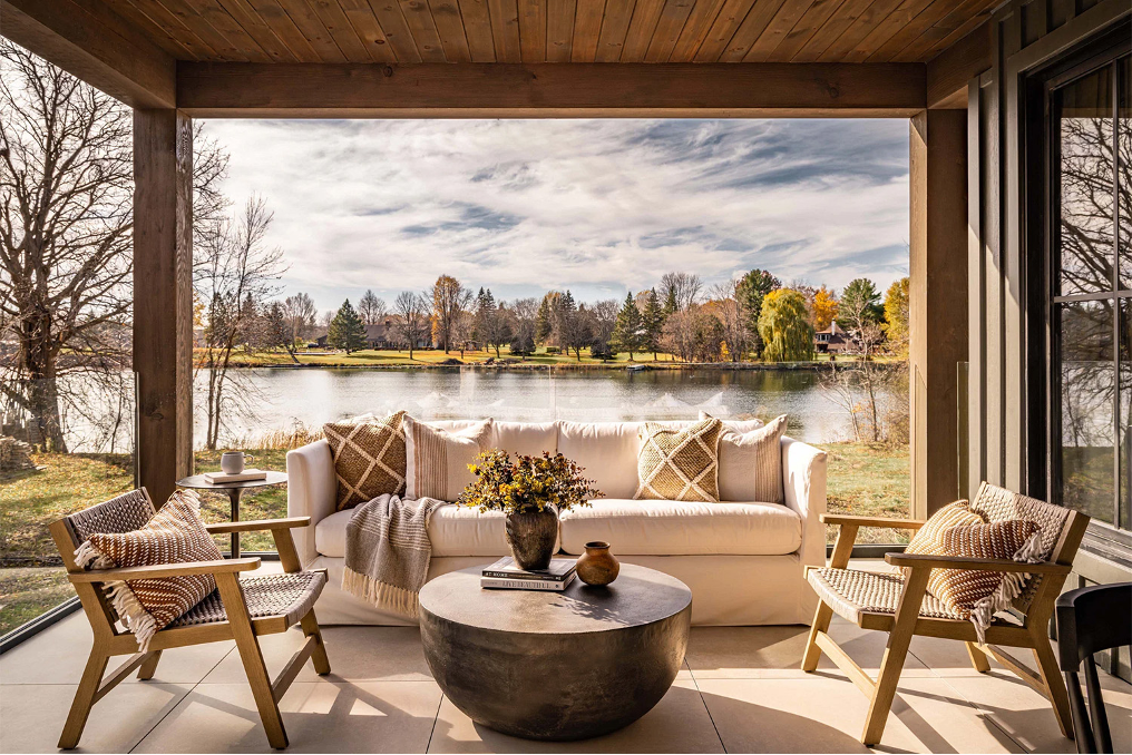 Covered patio with sofa, chairs, and round metal cocktail table with lake setting in background