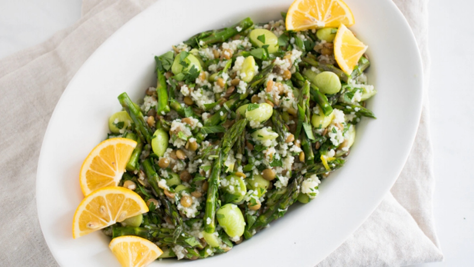 Spring Tabbouleh served on a white platter with fresh lemon wedges, asparagus, lentils, fava beans