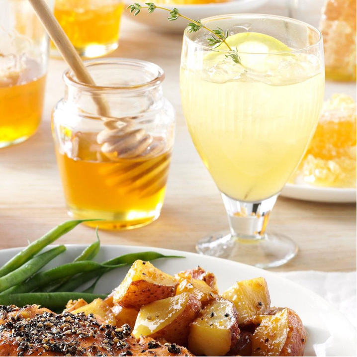 Glass of iced Grilled Lemon & Thyme Lemonade next to jar of honey and plate with green beans, roast potatoes